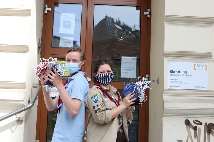 Pfadfinder Lukas und Pfadfinderin Saveria präsentieren die von ihrer Gruppe genähten und gespendeten Masken vor dem Tageszentrum Obdach Ester. (Bild: FSW)