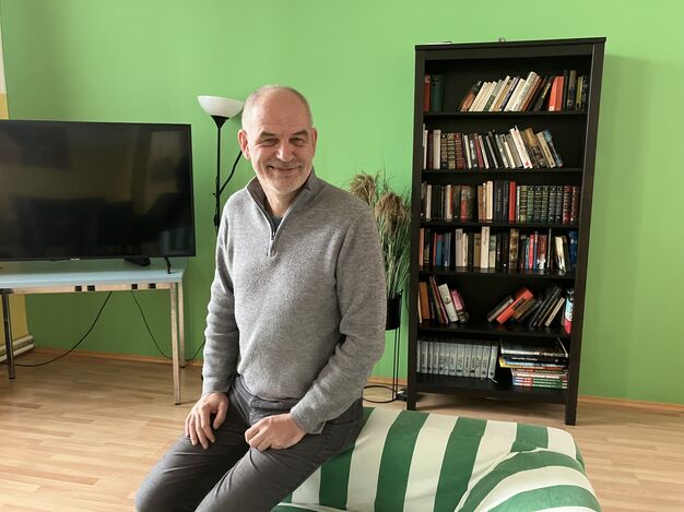 Stefan Stiglbauer lehnt am Sofa vor einer Bücherwand im Gemeinschaftsraum. 