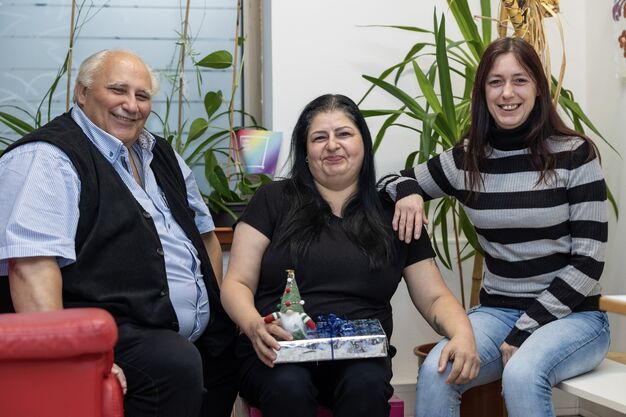 Franz Haberl (l.), Sonia und Lydia Potmesil (r.) in den Forum Obdach Räumlichkeiten auf einer Sitzlandschaft. Sonia hält ein Geschenk und eine Wichtelfigur.