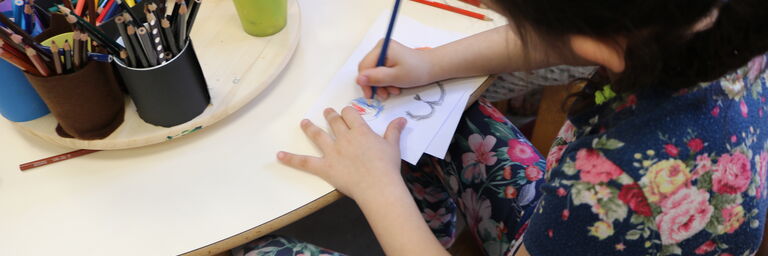 Ein Mädchen ist in der Kinderstube und zeichnet ein buntes Bild. (Bild: FSW)