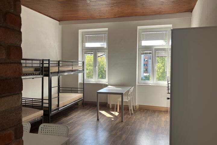 Betten, Tische, Kästen, Sessel: Alle Wohnungen sind mit den wichtigsten Möbeln ausgestattet. (Bild: FSW) Blick aus der Tür auf das helle Wohnzimmer mit Betten, einem Tisch und einem Kasten.
