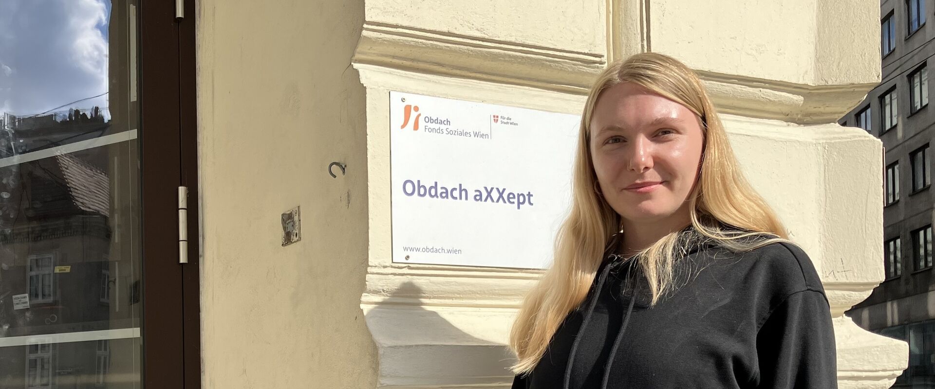 Diana Schmidt vor dem Schild neben der Eingangstür des Tageszentrums Obdach aXXept. 