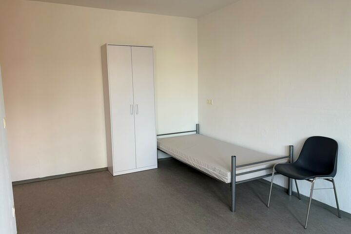 Ein weißer Kasten, ein Bett und ein schwarzer Sessel in einem Raum.