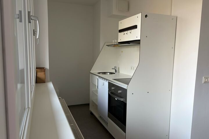 Eine kleine weiße Kochecke mit Herd, Kästen und Abwasch. 