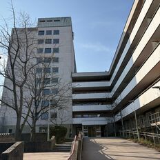 Wohnhaus vor blauem Himmel, Bäumen im Vordergrund und dem Haupteingang. 