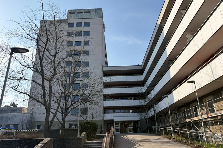 Wohnhaus vor blauem Himmel, Bäumen im Vordergrund und dem Haupteingang. 