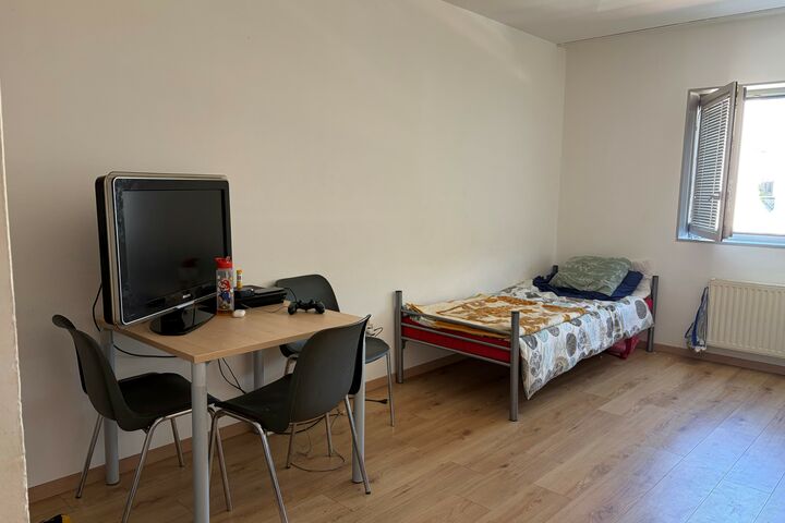 Ein Tisch mit einem Fernseher, Sessel und ein bezogenes Bett in einem Zimmer. 